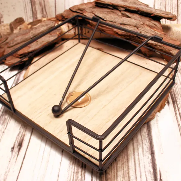 Quadratischer Serviettenhalter aus schwarzem Metall-Zaun und hellem Holz mit einem Kugel-Gewichtarm auf einer Baumscheibe.