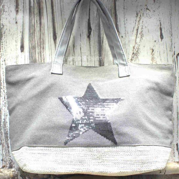 Große graue Shoppertasche mit silbernem Pailletten-Stern, weißem Boden-Element und grauen Kunstleder-Tragegriffen vor rustikalem Holzhintergrund.