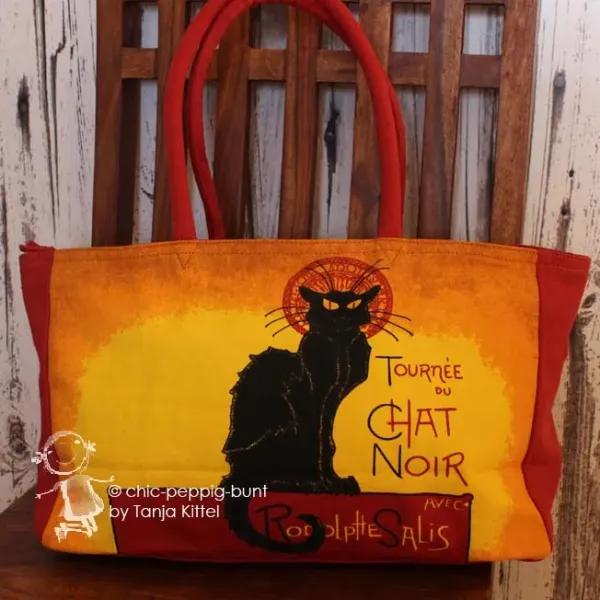 Stoff-Shoppertasche Chat Noir in Gelb und Rot mit Motiv einer schwarzen Katze, Reißverschluss und roten Tragegriffen.