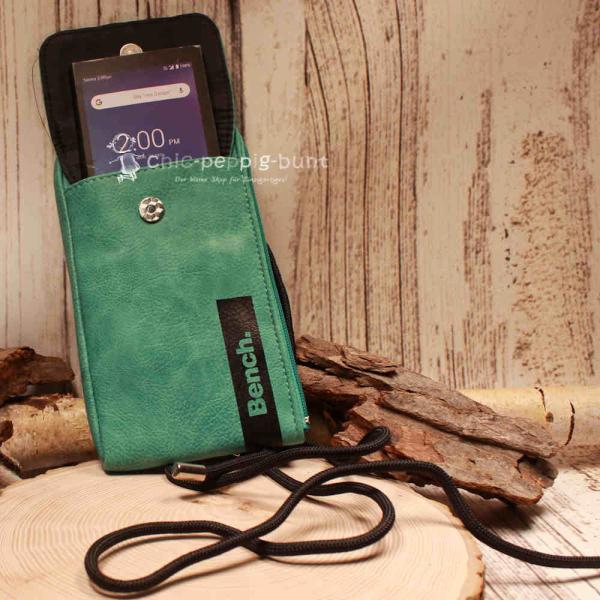 Flache grüne Bench Handtasche auf Holzuntergrund mit Maßen 21 x 12 x 2 cm.