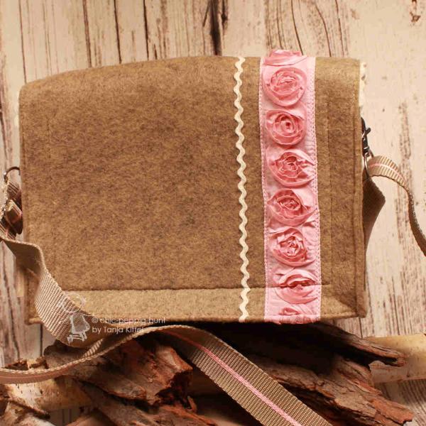 Rückseite der Filztasche aus hellbraunem Stoff mit der vertikal aufgenähten, rosafarbenen Rosenbordüre und dem Schultergurt.