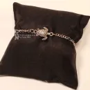 Versilbertes Gliederarmband mit ausgearbeiteter silberfarbener Schildkröte auf einem schwarzen Schmuckkissen.