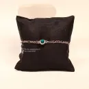 Versilbertes Gliederarmband mit leuchtendem türkisblauem Swarovski Stein präsentiert auf einem schwarzen Schmuckkissen.