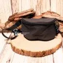 Vorderansicht der kleinen schwarzen Stoff-Gürteltasche für Kinder auf einer rustikalen Holzscheibe präsentiert.