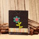 Handgenähte dunkelgraue Filz Passhülle der Marke Weidräwöl mit blauer Blumen-Applikation und bunt gestreifter Bordüre für Reisepass und Impfpass.