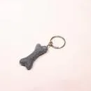 Handgefertigter Mini Knochen aus blauem Filz als witziger Schlüsselanhänger und weicher Taschenbaumler, hängend und liegend dargestellt.