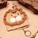 Gehäkelter Löwe Schlüsselanhänger in Beige mit brauner Mähne, grüner Schnur und rosa Perle auf einer Holzscheibe.