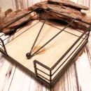 Quadratischer Serviettenhalter aus schwarzem Metall-Zaun und hellem Holz mit einem Kugel-Gewichtarm auf einer Baumscheibe.