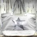 Große graue Shoppertasche mit silbernem Pailletten-Stern, weißem Boden-Element und grauen Kunstleder-Tragegriffen vor rustikalem Holzhintergrund.