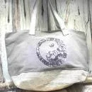 Graue Shoppertasche mit silbernem Yin Yang Pailletten-Motiv, weißem Boden mit Silberstreifen und grauen Kunstleder-Griffen vor Holz-Hintergrund.