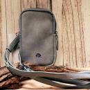 Kleine grau-blaue Leder-Umhängetasche mit verstellbarem Gurt, Karabinerhaken und Reißverschlussfächern auf hellem Holzgrund.